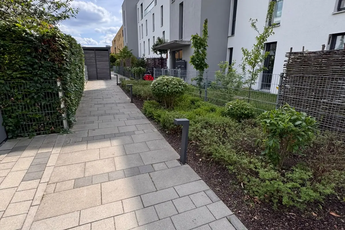 Gepflasterter Weg mit Bepflanzung entlang einer Wohnanlage